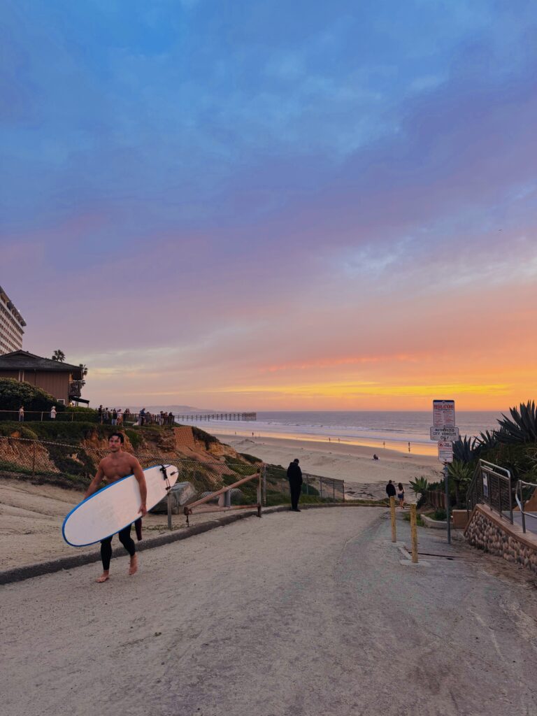 Pacific beach sunset with surfer walking with surf board