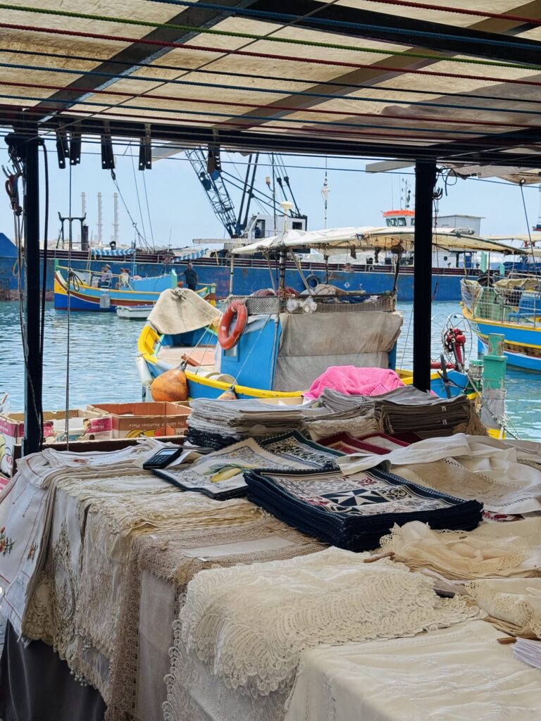Fabric vendor in Marsaxlokk with fishing boats in the harbor
