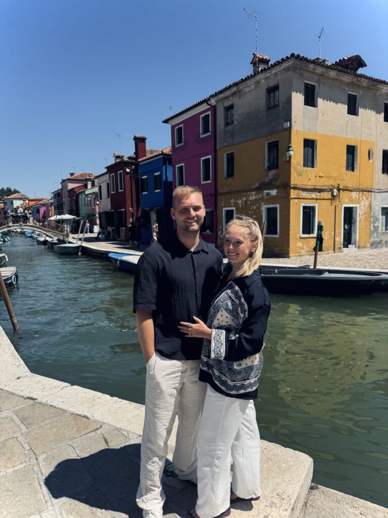Couple posing in front of colorful houses along canal in the quaint village of Burano in Italy